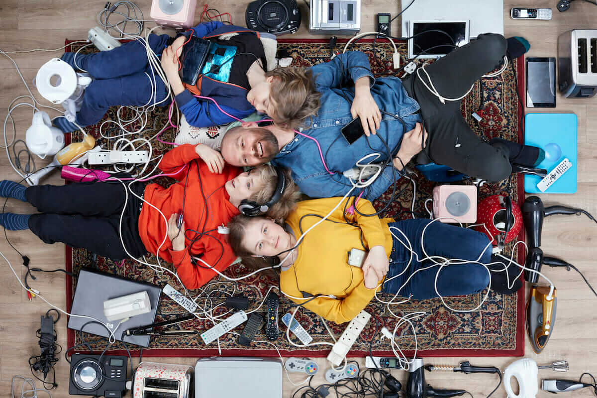 A father and three pale skinned children lying in a pile of old electrical items