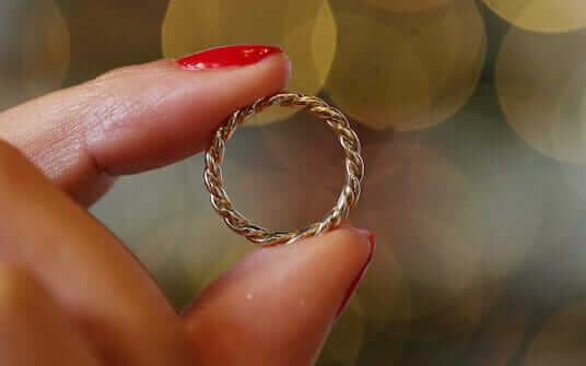 close up of a medium skinned womans fingers with red nail polish holding a ring made by Lylie's from recycled electricals