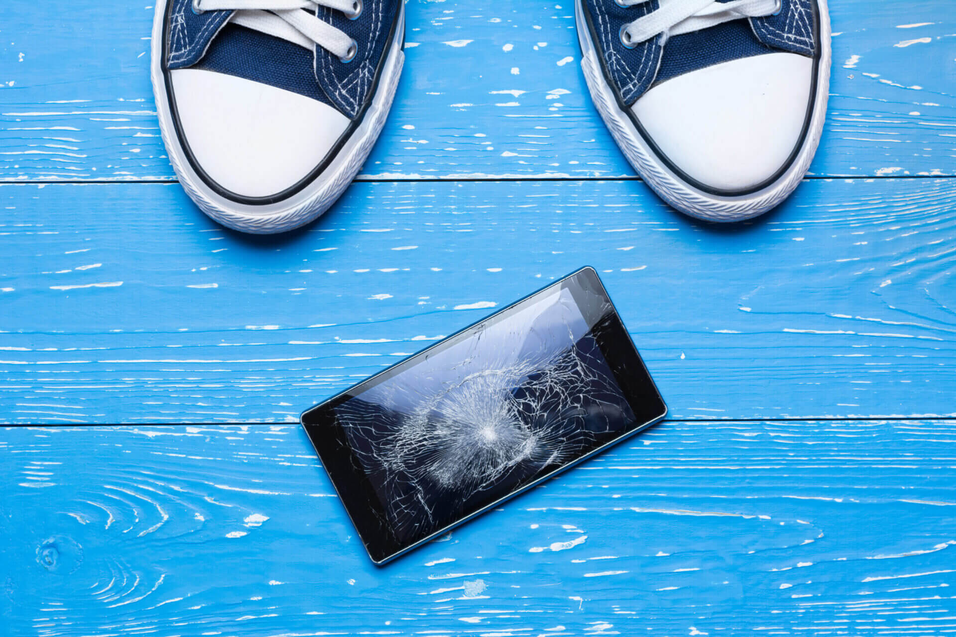 Mobile,Phone,With,Broken,Screen,On,Floor,Concept mobile phone aon a blue floor with the toes of a pair of sneakers showing