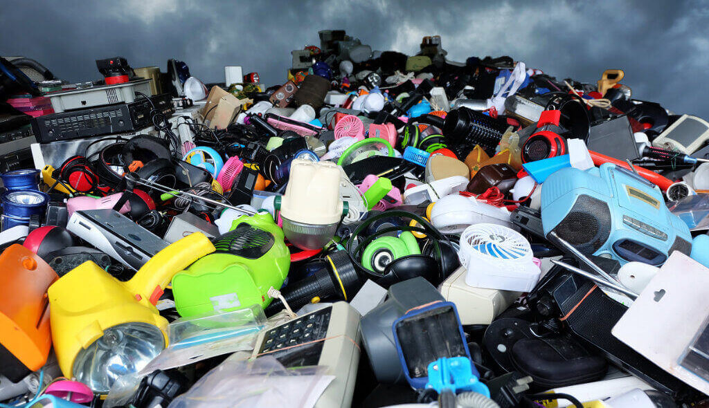 Looking up at a mountainous pile of colourful waste electricals against a stormy sky.