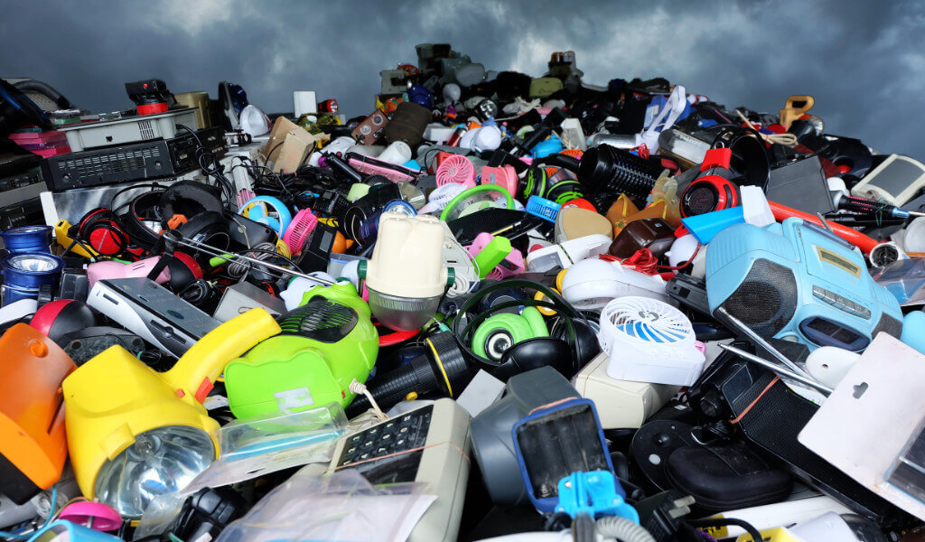 Looking up at a mountainous pile of colourful waste electricals against a stormy sky.