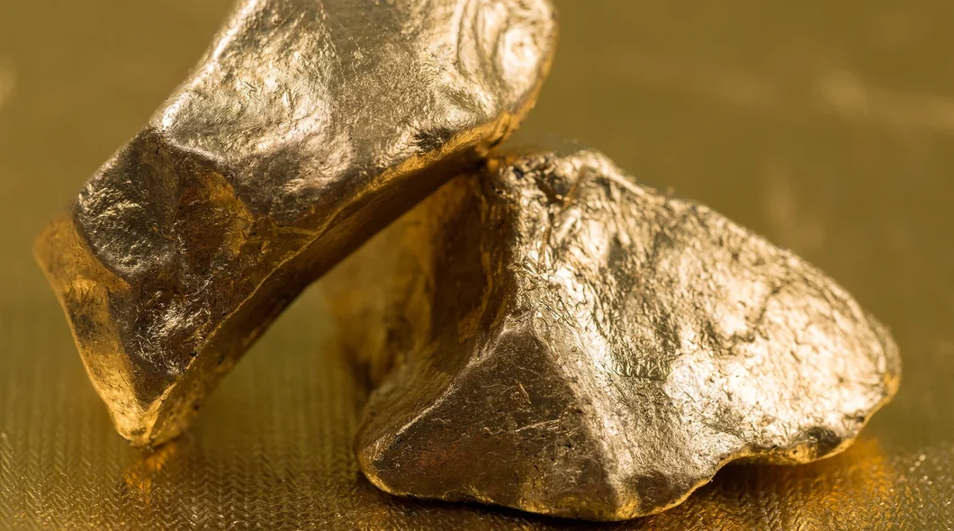 Close up shot of two lumps of gold on a shiny gold surface.
