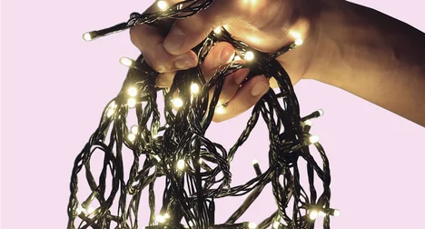 a close up of some christmas tree lights being held by a pale skinned hand on a plain background
