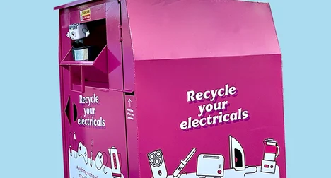 Bright pink recycling bring bank against a pale blue backdrop. Text on bank 'Recycle your electricals'.