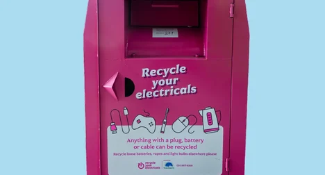 Bright pink recycling bring bank against a pale blue backdrop. Text on bank 'Recycle your electricals'.