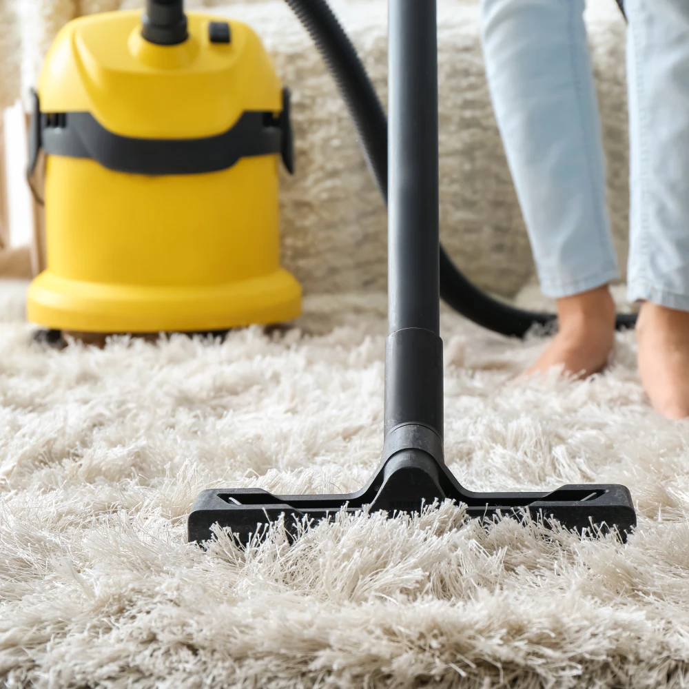 cropped front view of someone bare foot vacuuming a shag-pile rug with a black and yellow two part vacuum